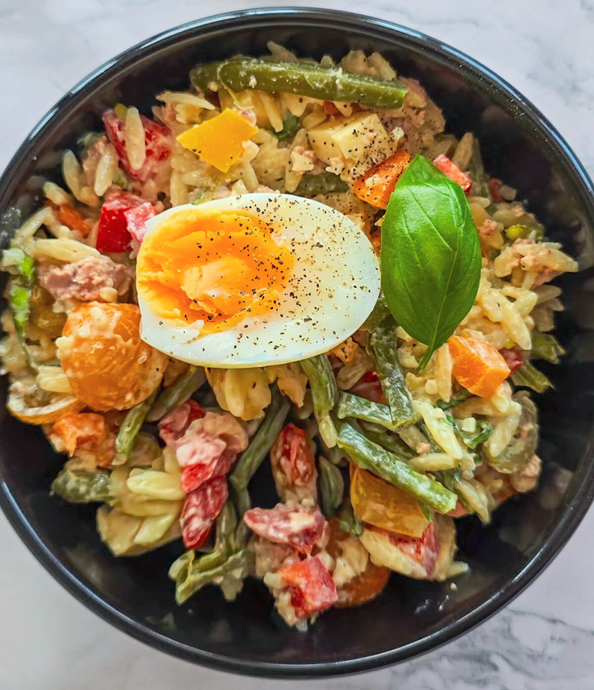 Une salade d'orzo méditerranéenne dans un bol noir.