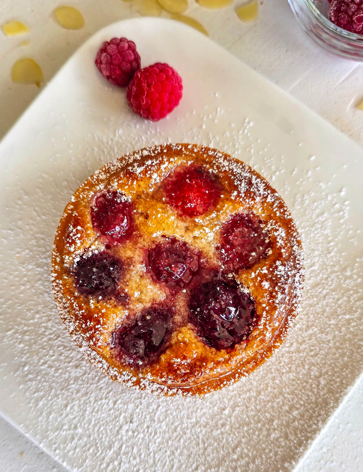 Une tartelette framboise sur une assiette blanche, avec un peu de sucre glace.