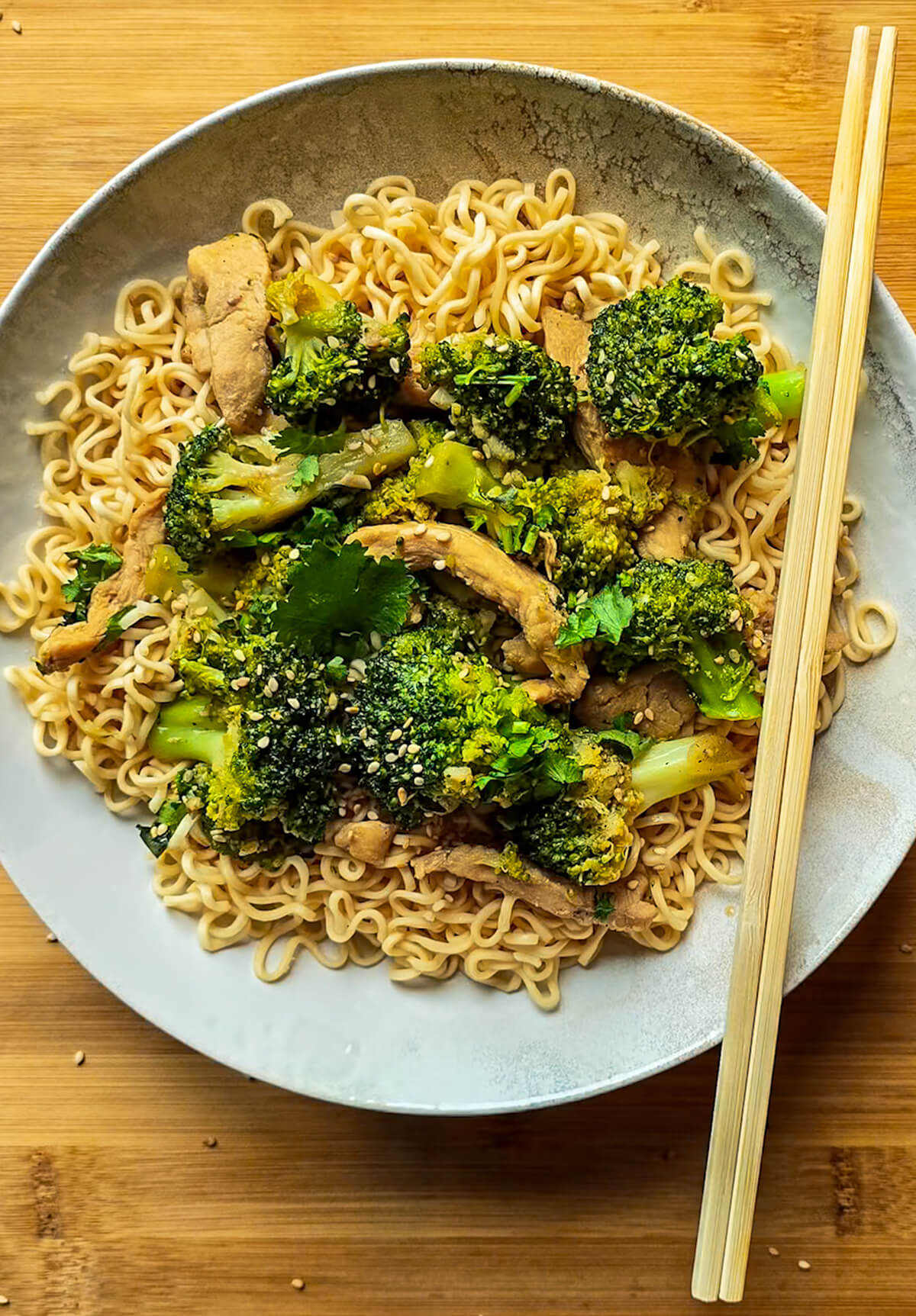 Des nouilles sautées au poulet avec des baguettes chinoises, dans une assiette creuse blanche.