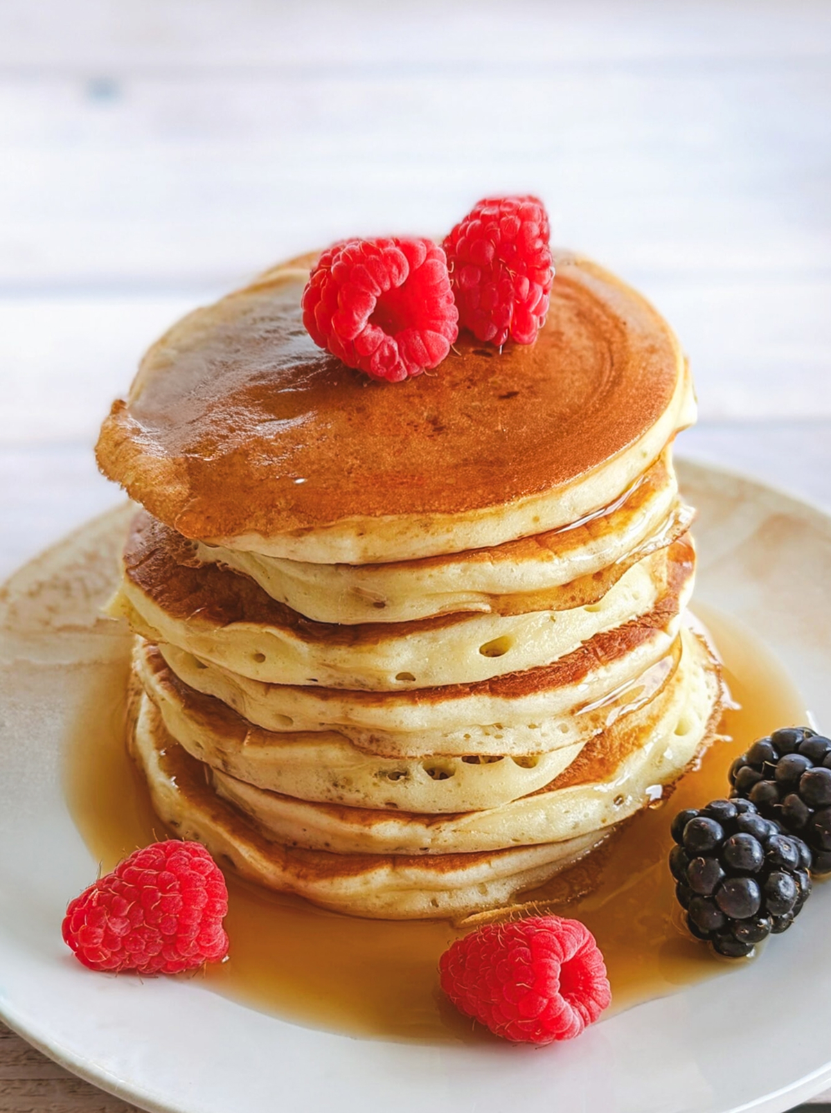 Des pancakes fluffy (moelleux) dans une assiette blanche, avec du sirop d'érable et des fruits rouges.