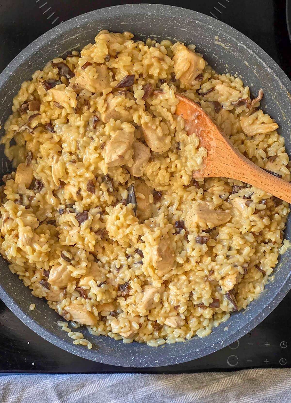 Du risotto poulet champignons dans une poêle, cuillère en bois sur le côté.