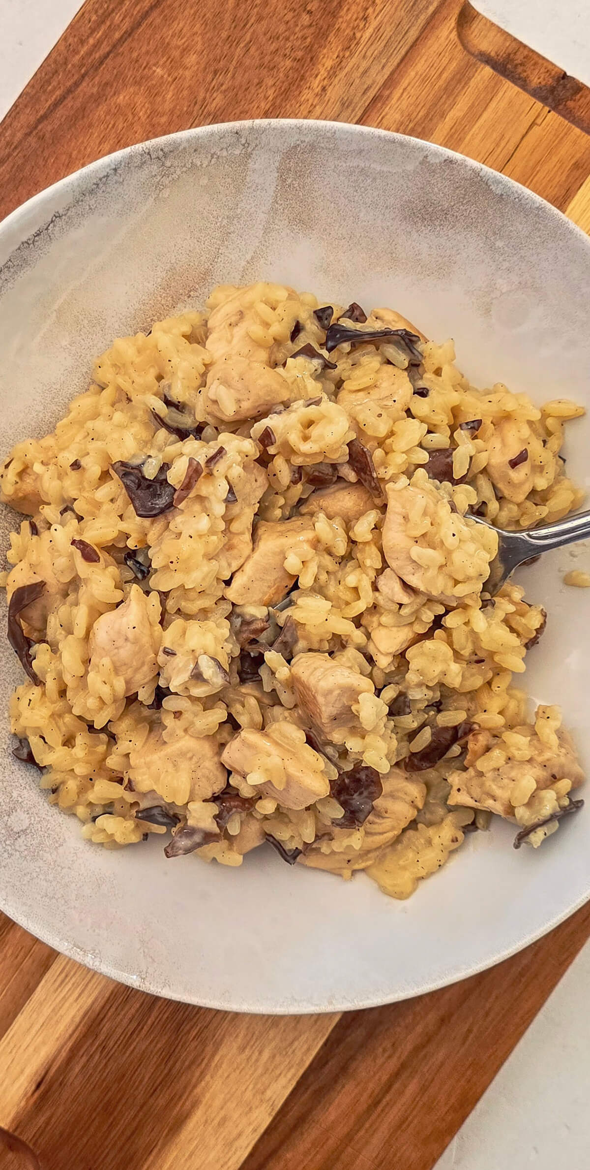 Une assiette beige remplie de risotto poulet champignons, fourchette sur le côté
