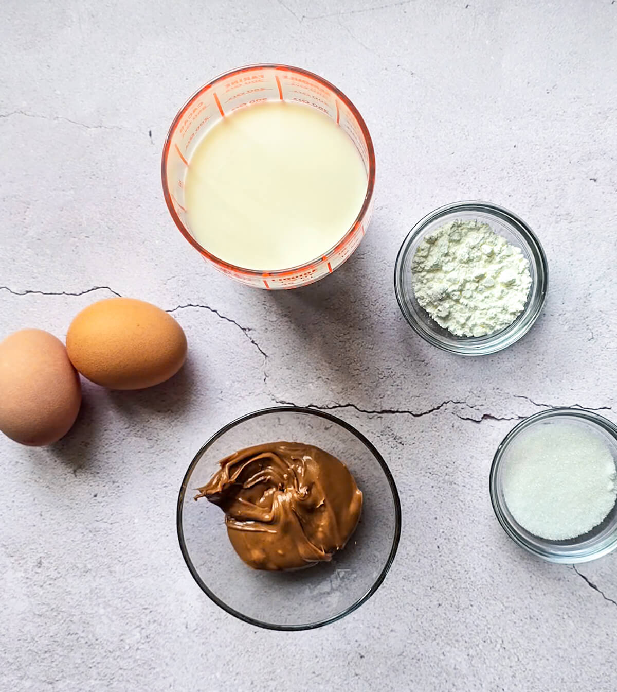 Des ingrédients pour faire des crèmes dessert praliné, sur un fond gris clair.