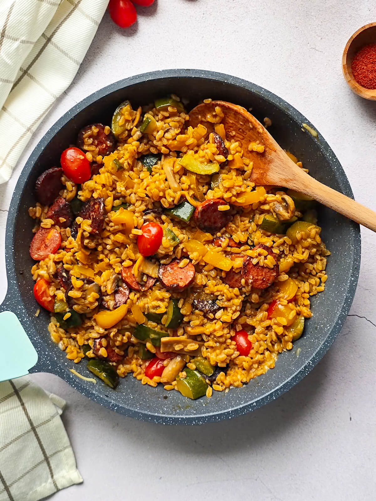 Une poele contenant des ingrédients avec une cuillère en bois, pour une recette de one pot blé chorizo.