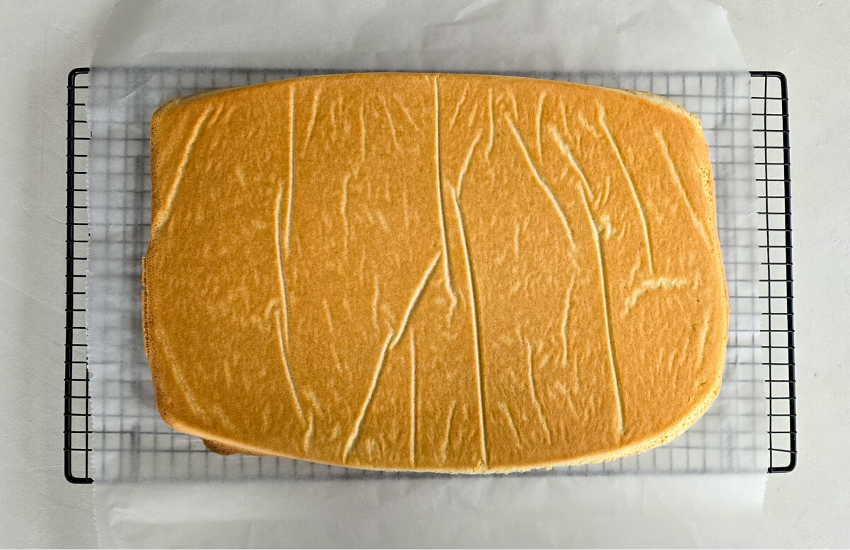 Baked Joconde sponge cooling on a wire rack against a clean white background.