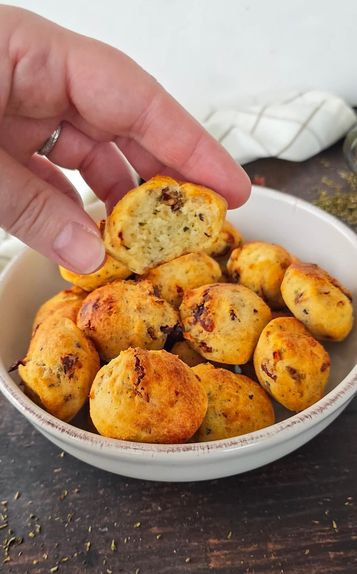 Une main tenant une madeleine moelleuse tomates séchées parmesan.