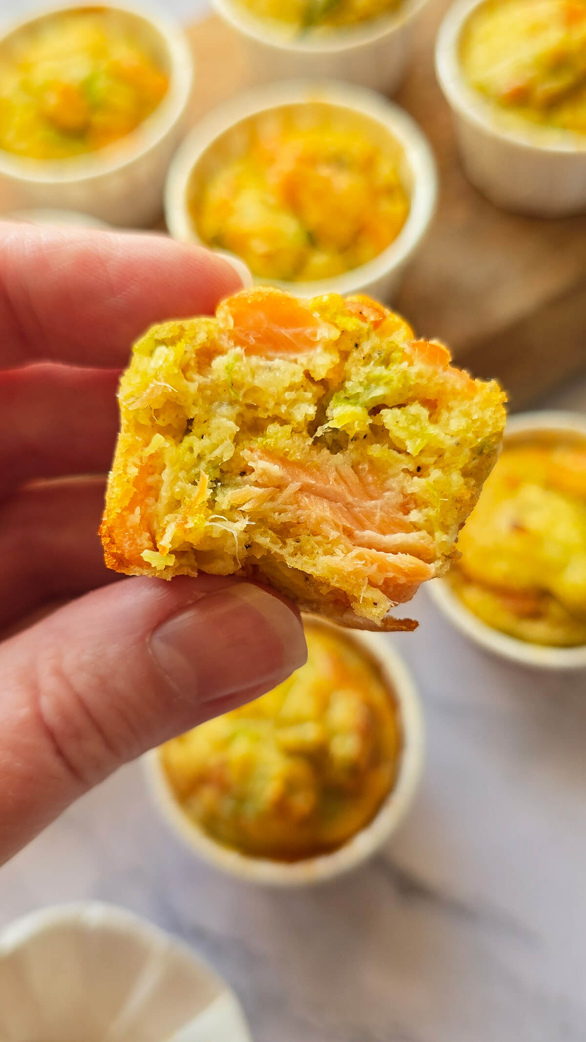 Une main tenant un morceau de muffins poireaux et saumon.