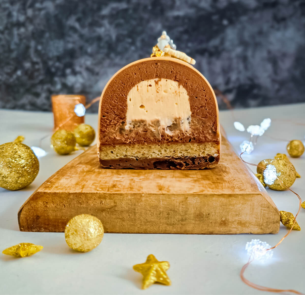 Une Bûche de Noël poire caramel découpée sur une planche de bois, avec des décorations autour.