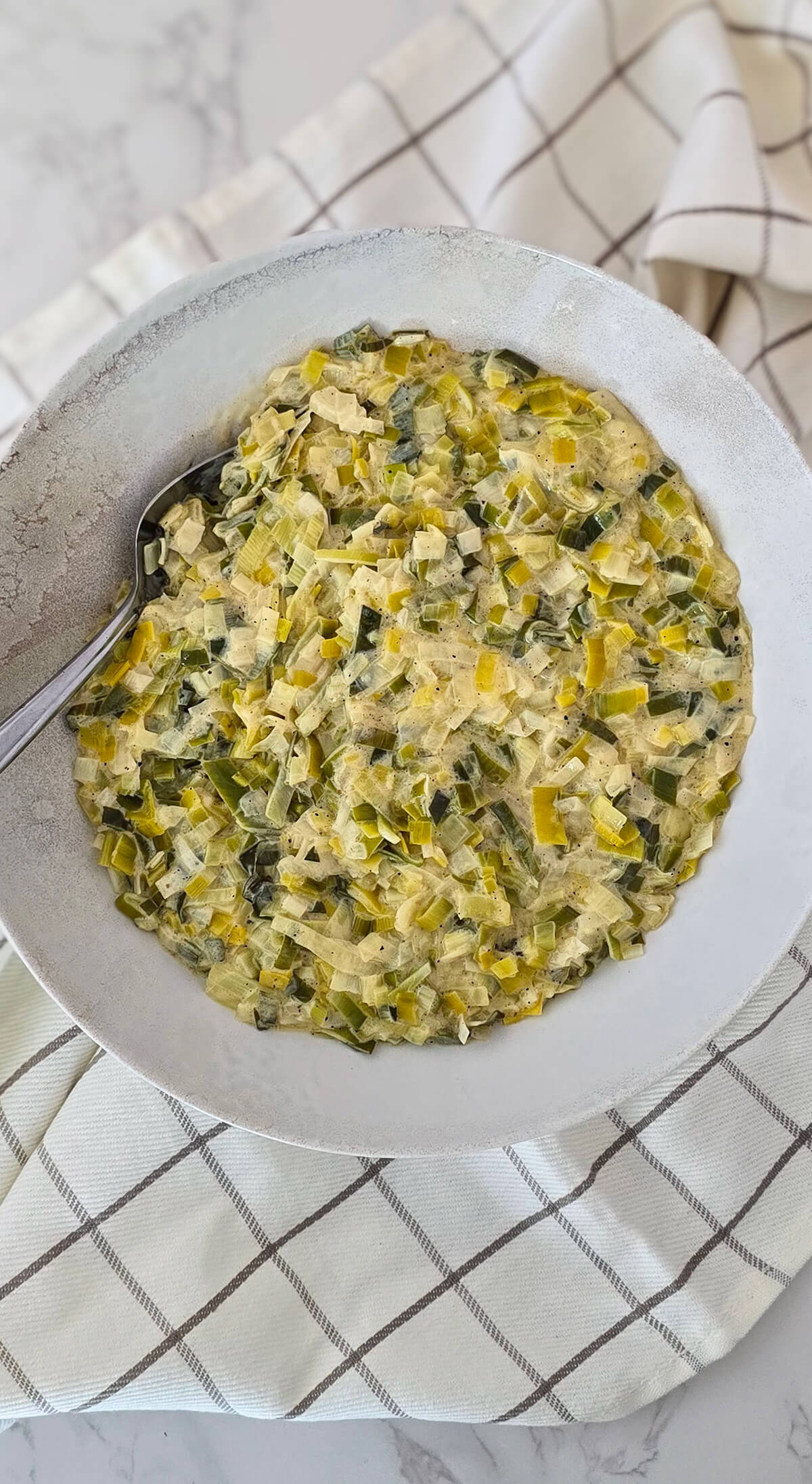 Une fondue de poireaux dans un plat de présentation blanc, avec un torchon.