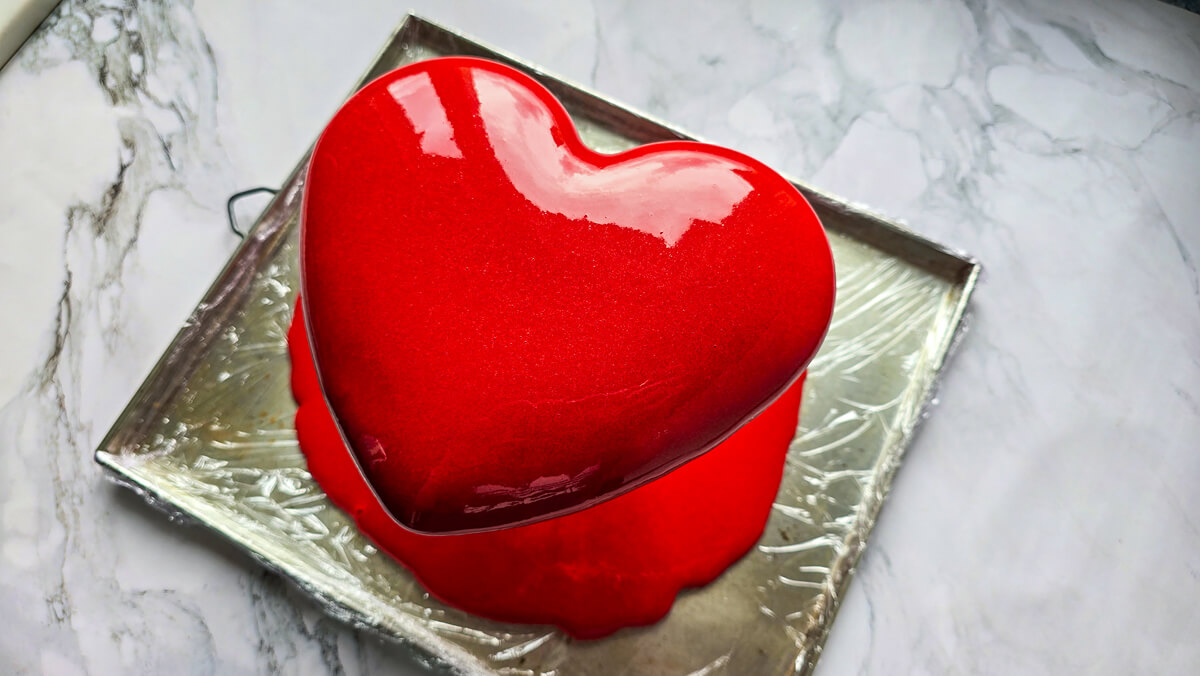 Un glaçage miroir rouge versé sur un entremets fraise et chocolat blanc.