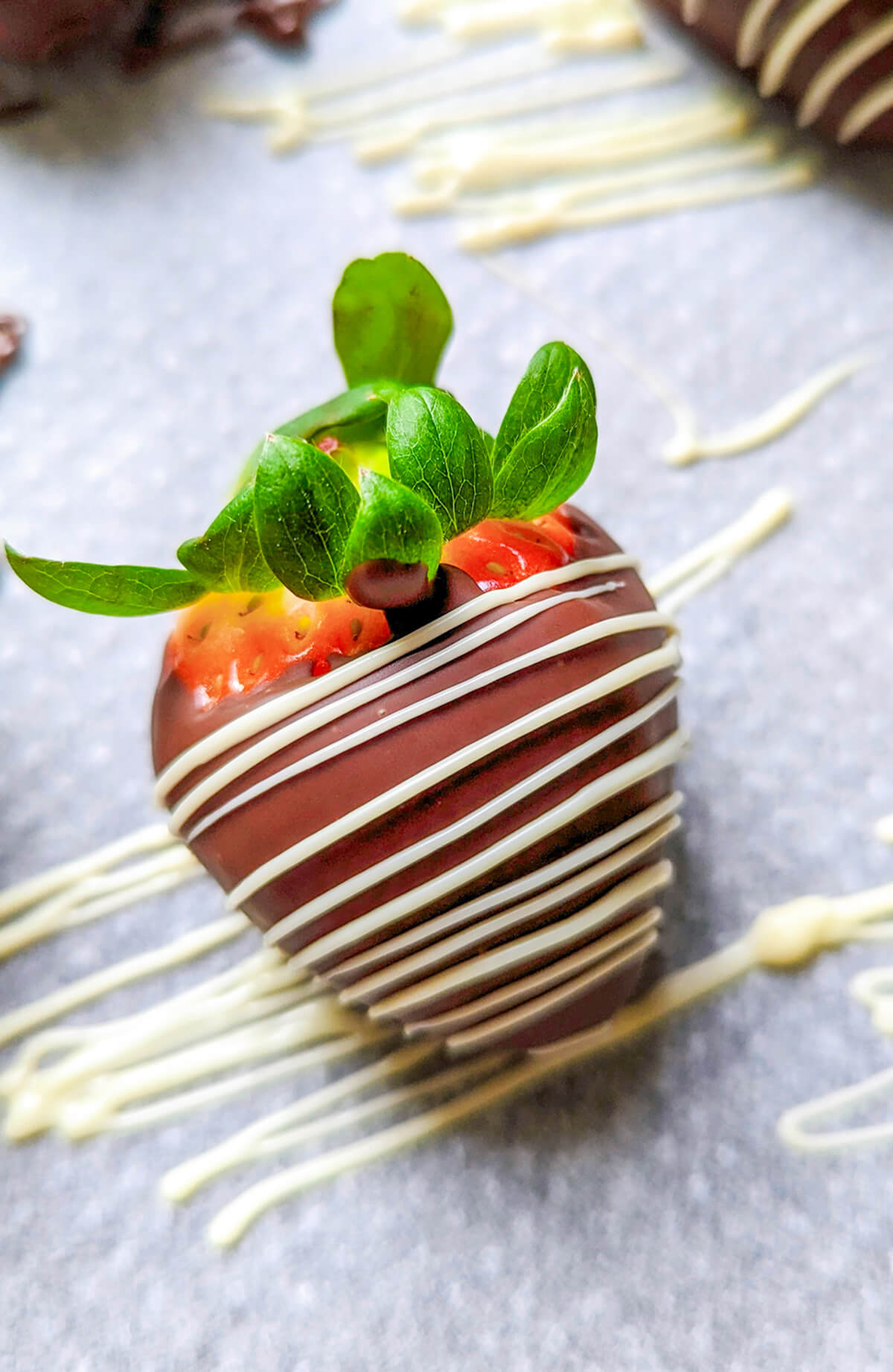 Une fraise enrobée de chocolat au lait avec un filet de chocolat blanc.
