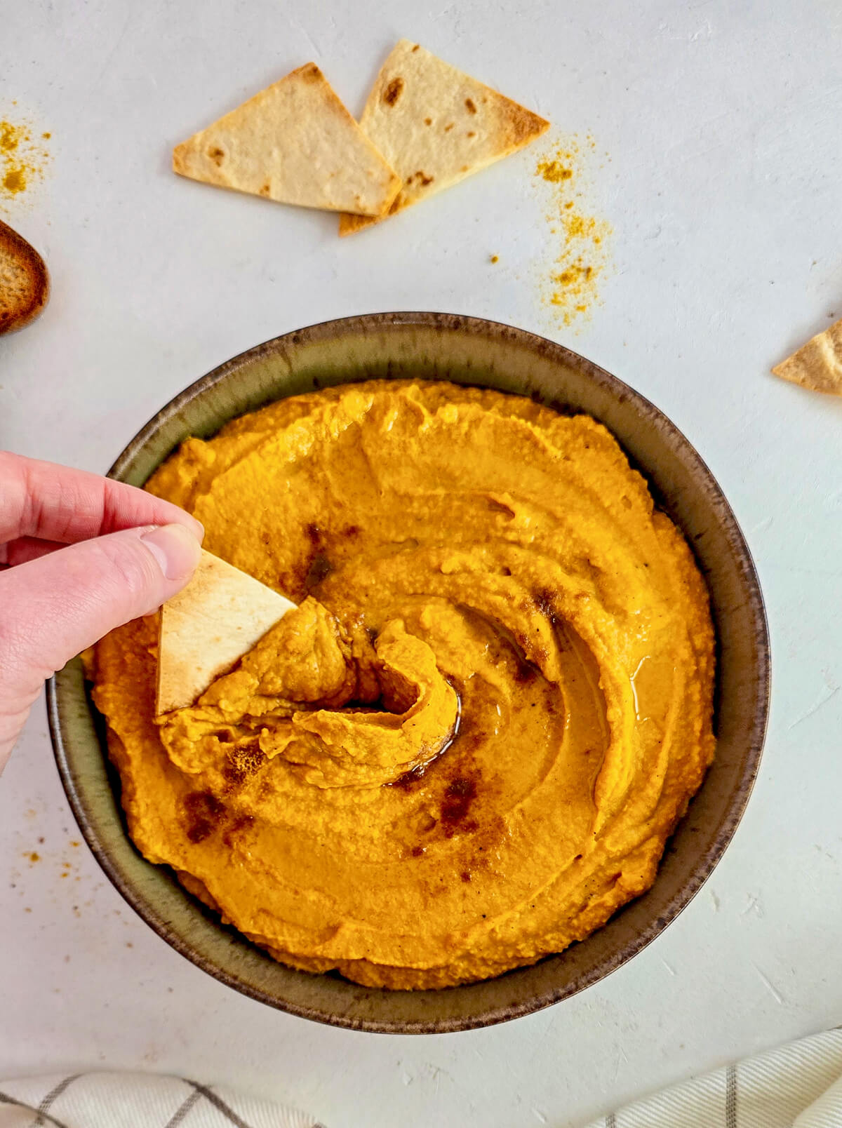 Une chips de pita dans du houmous, sur un fond blanc.