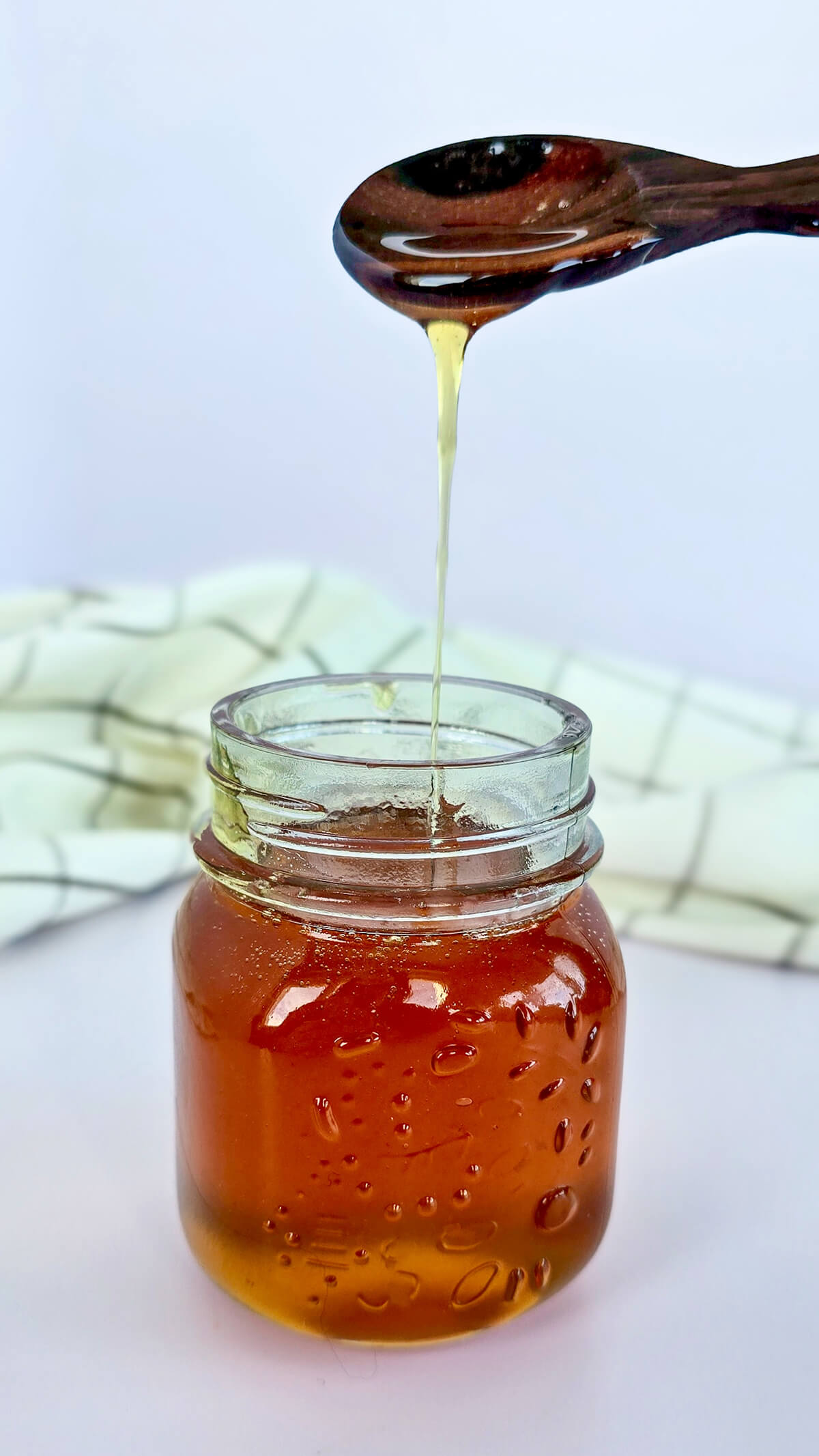 Filet de caramel liquide maison coulant d'une cuillère en bois dans un bocal en verre.
