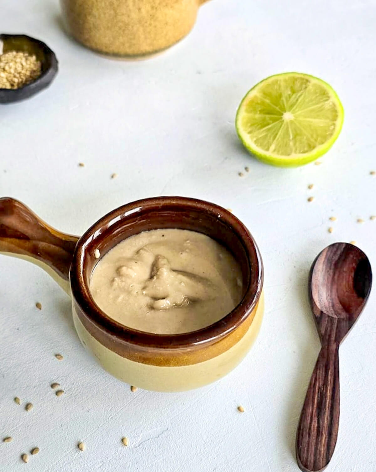 Un contenant marron avec du tahini et une moitié de citron vert.