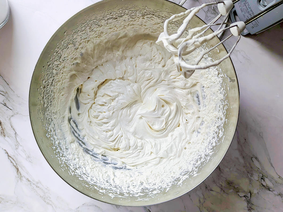 Une crème chantilly fait maison dans un récipient, fouet sur le côté.