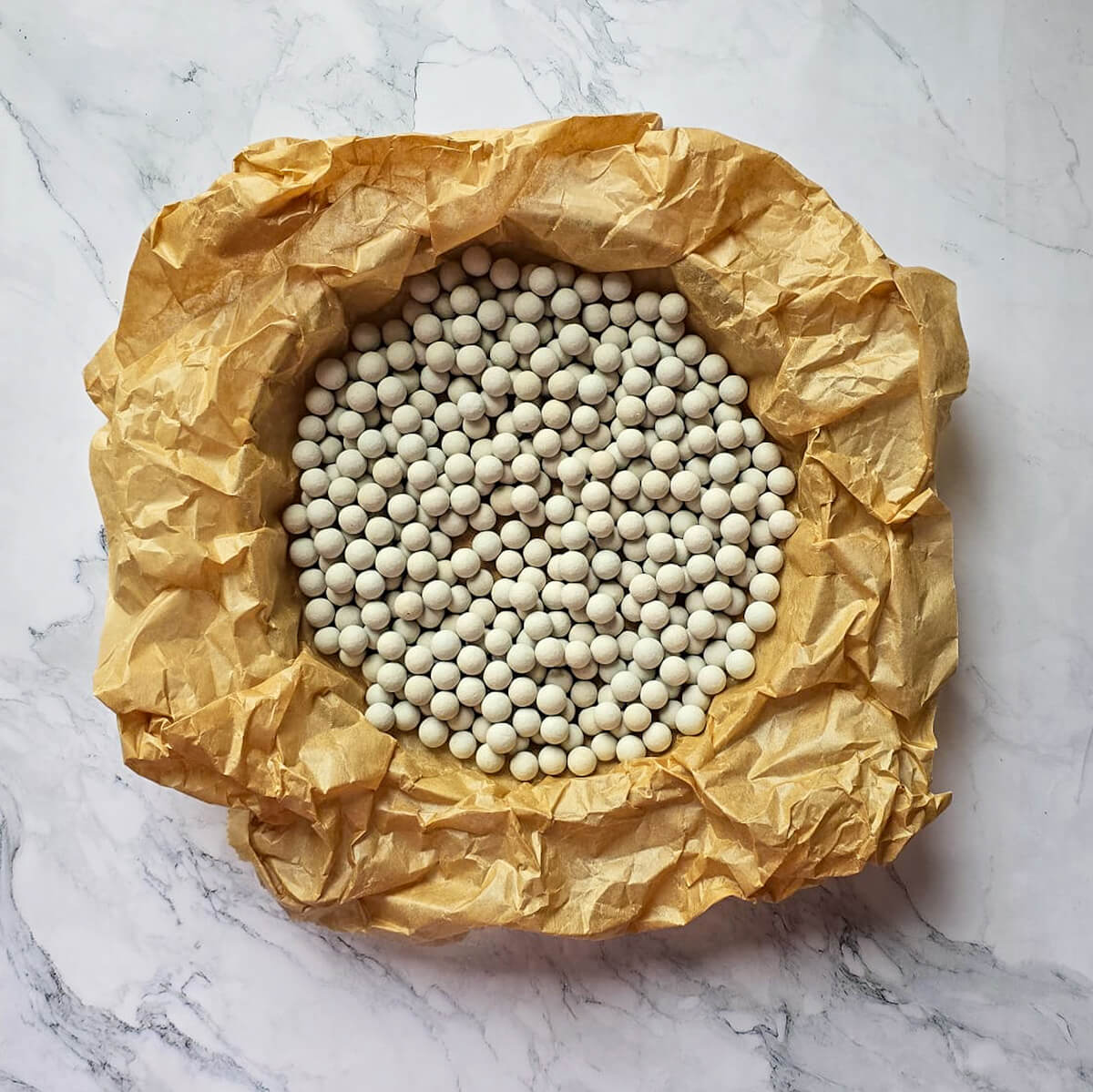 Des billes céramiques spécial cuisson à blanc pour une tarte, avec du papier sulfurisé.