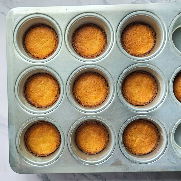 Palets bretons dorés après cuisson dans un moule à muffins en métal, montrant une bordure croustillante et un centre moelleux.