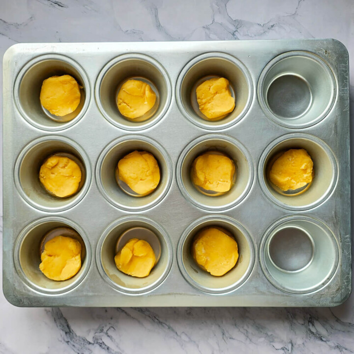Boules de pâte à palets bretons déposées dans les empreintes d'un moule à muffins en métal pour une cuisson parfaitement régulière.