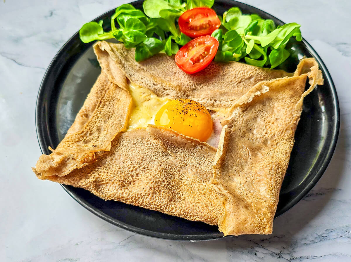 Photo d'une galette de sarrasin croustillante garnie d'un œuf miroir et de fromage.