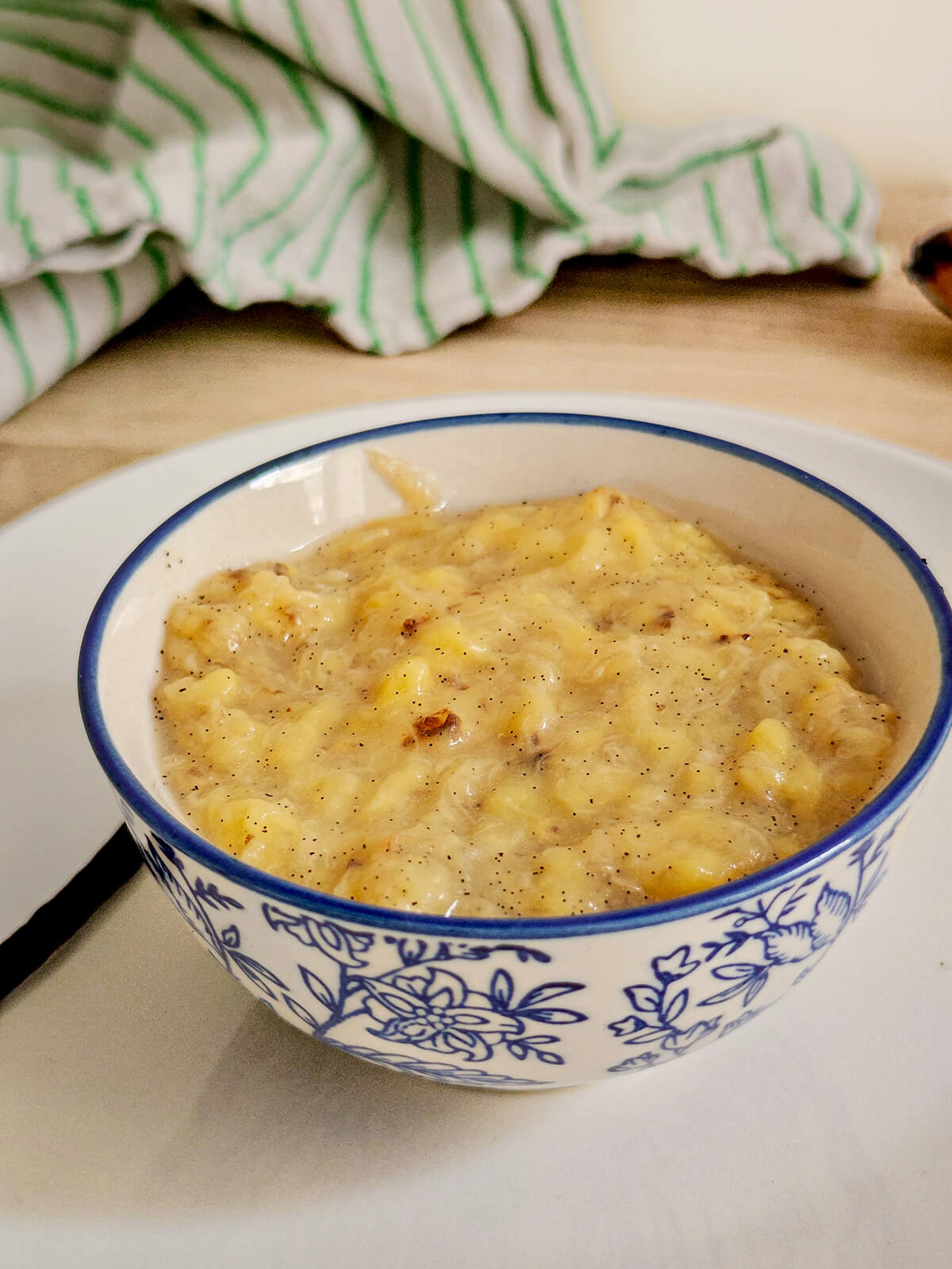 Bol de compote de banane à la vanille avec une gousse de vanille sur le rebord et une banane mûre en arrière-plan.