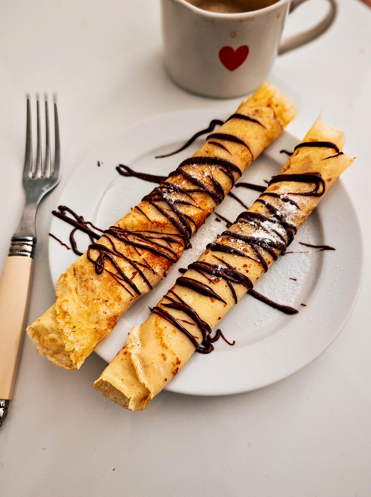 Des crêpes avec un filet de pâte à tartiner dans une assiette, idéal pour la Chandeleur.