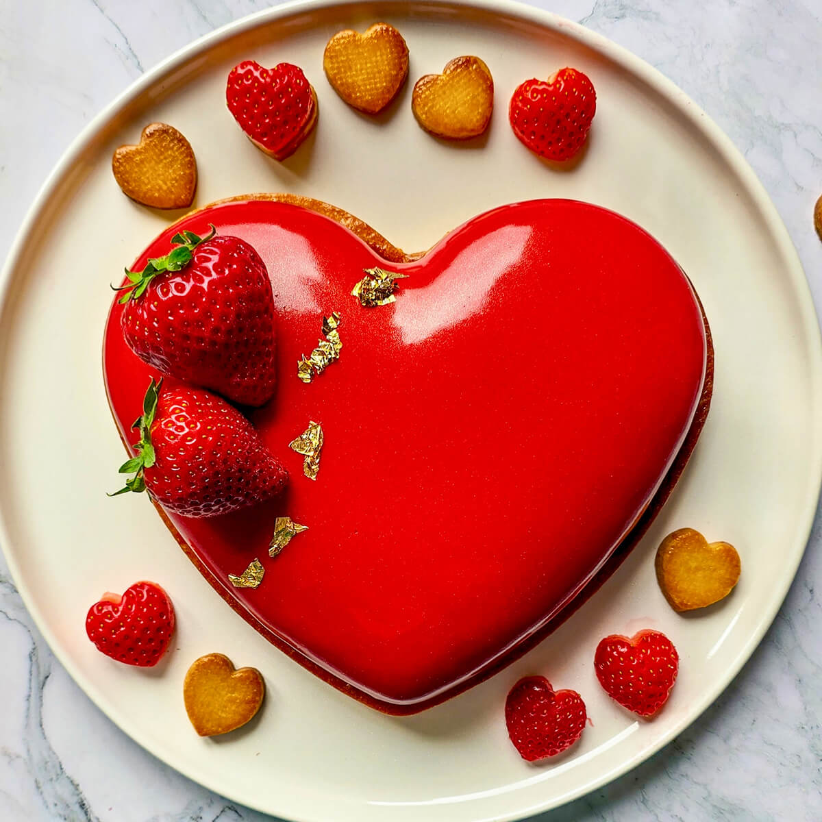 Un entremets fraise avec un glaçage miroir transparent sur une assiette blanche.