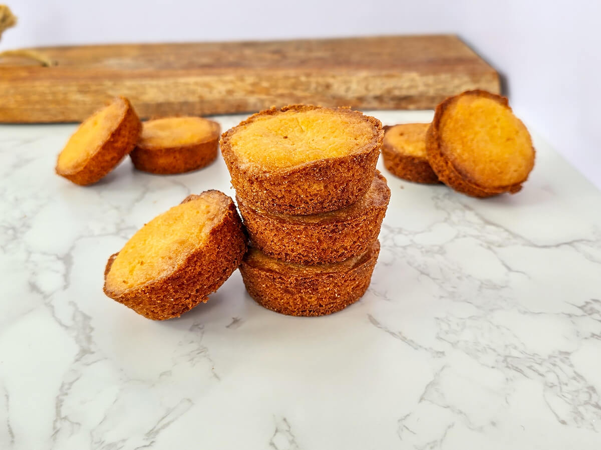 Biscuits palets bretons artisanaux pur beurre présentés sur un marbre blanc avec une planche en bois en arrière-plan, texture dorée et sablée typique de la pâtisserie bretonne.