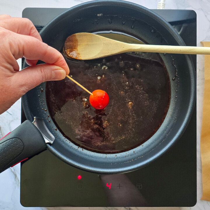Ume main qui trempe une tomate cerise dans du caramel.