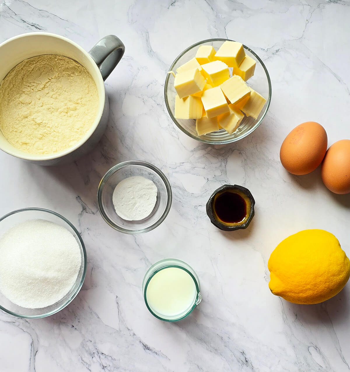 Des ingrédients pour faire des cupcakes vanille en forme de roses, sur un fond marbré blanc.