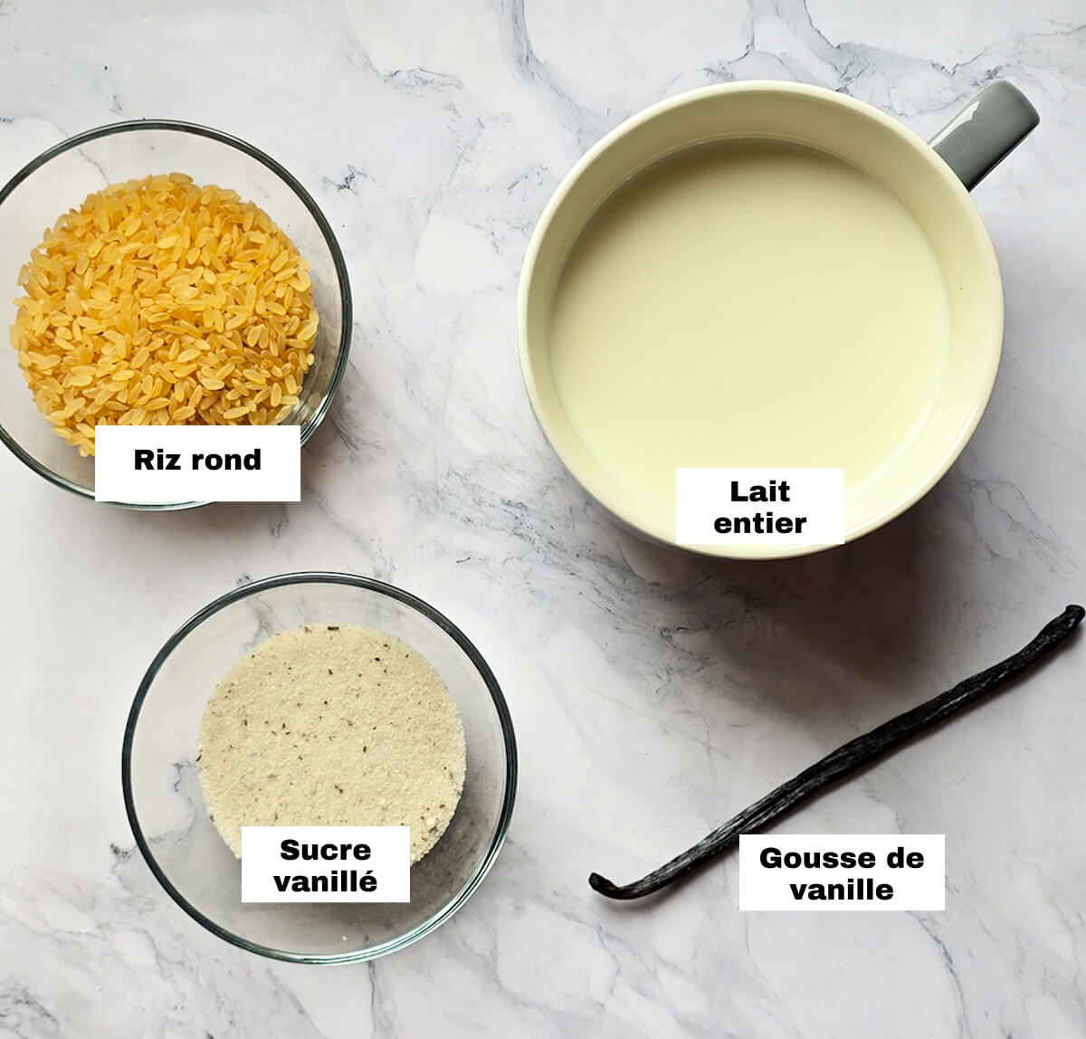 Les ingrédients pour faire du riz au lait à la vanille sur un fond blanc marbré.