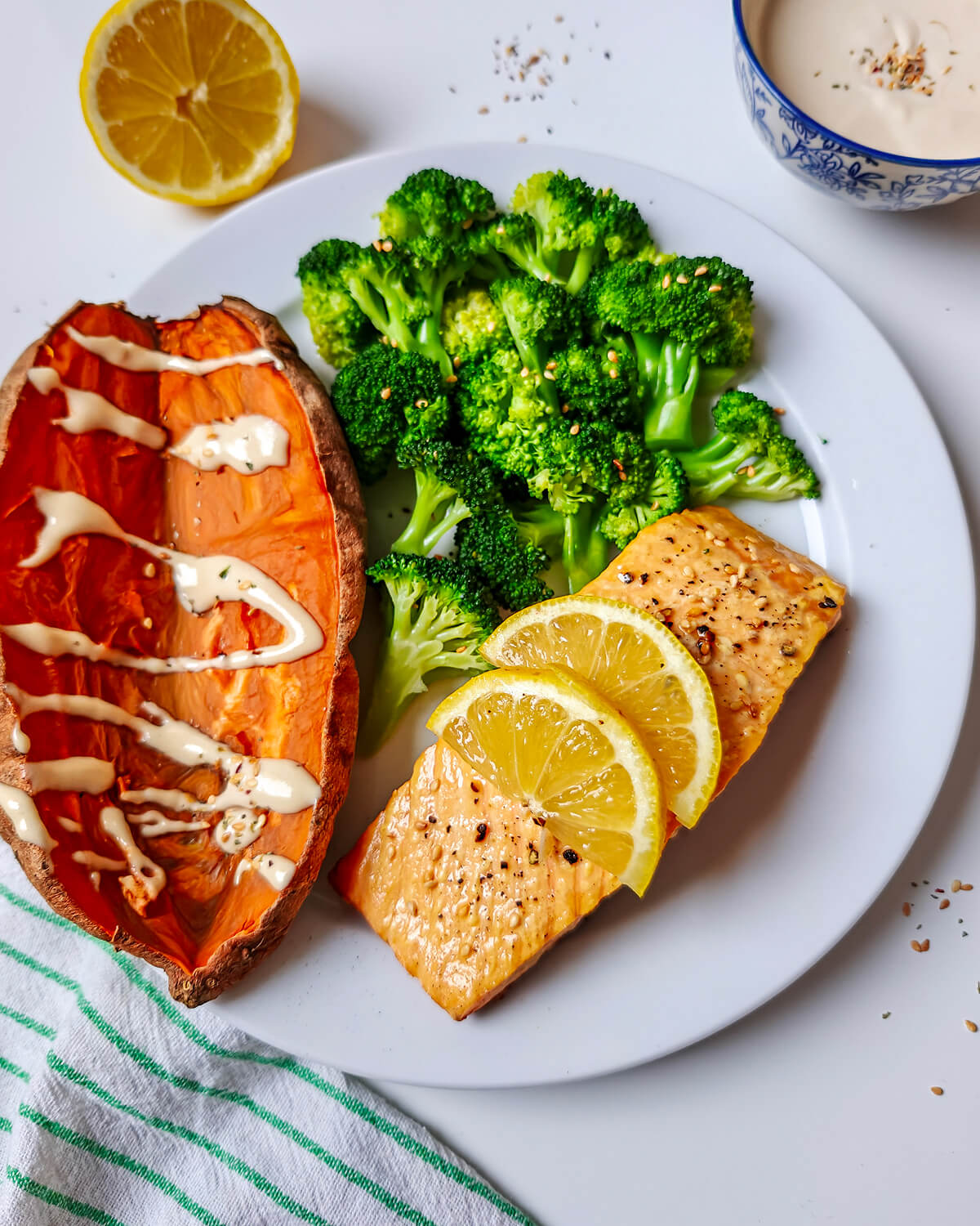 Assiette équilibrée composée d'un pavé de saumon patates douces aux zestes de citron, d'une demi-patate douce rôtie avec une sauce blanche et de brocolis vapeur parsemés de sésame.