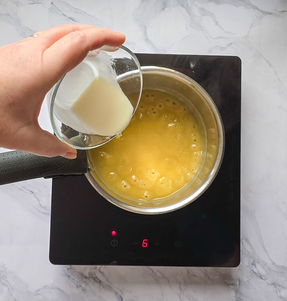 Une main ajoutant des ingrédients dans une casserole contenant de la purée de poire pour la préparation d'un curd poire.