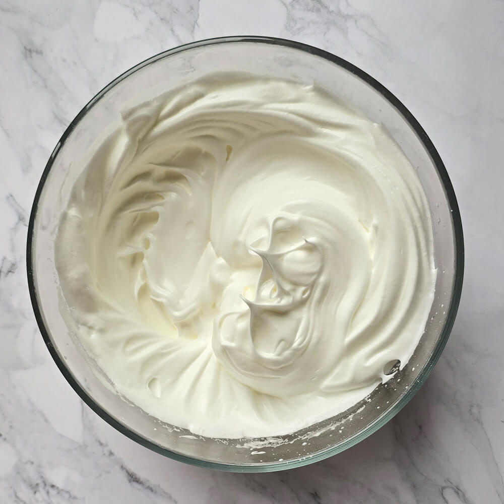 Saladier en verre rempli de blancs d'œufs montés en neige bien fermes et brillants, formant des pics, prêt pour une recette d'île flottante.