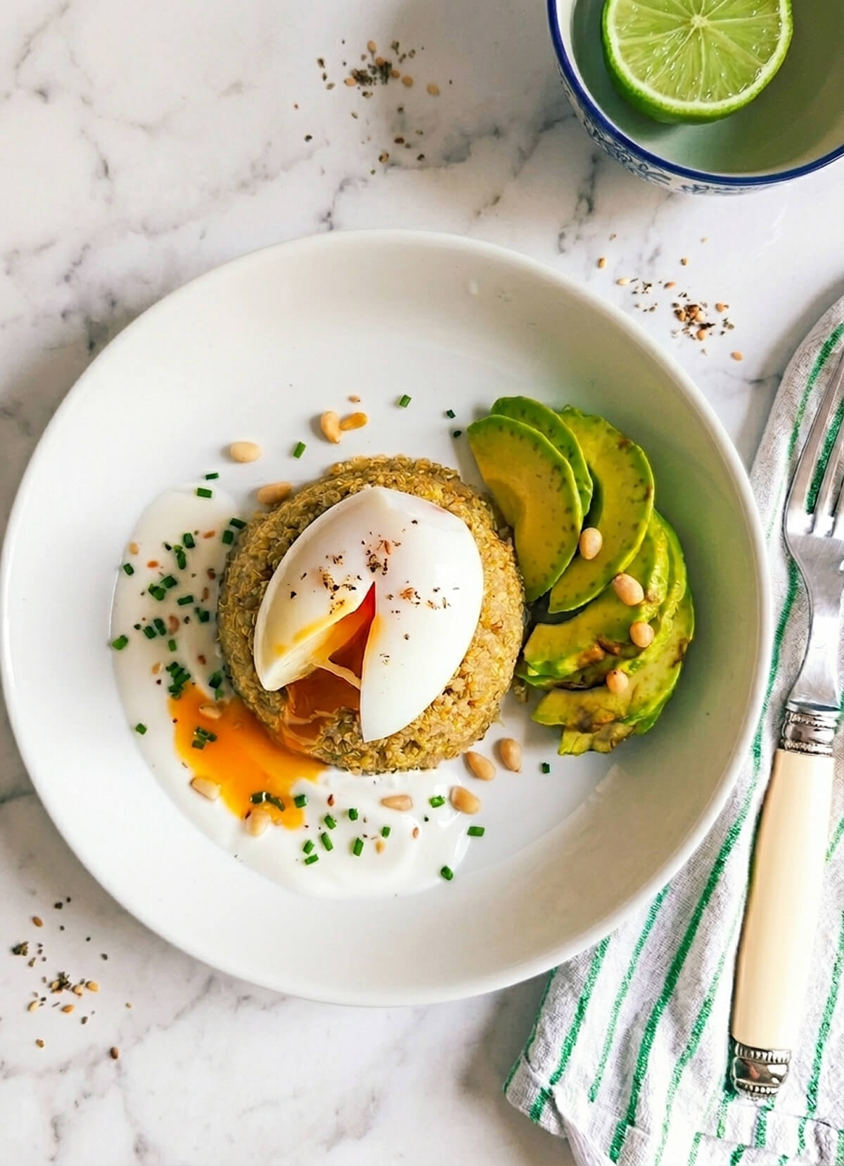 Un bowl de quinoa, avocat et oeuf mollet dans une assiette blanche, fond marbré, fourchette et torchon sur le côté.