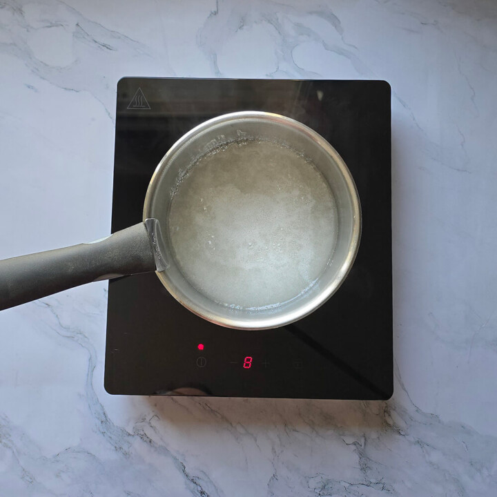 Préparation d'un caramel liquide dans une casserole, sur un fond blanc marbré.