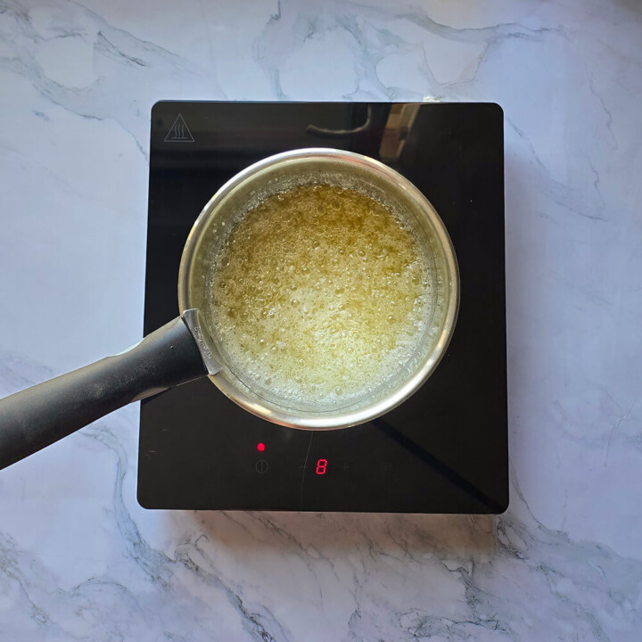 Coloration (caramélisation) du caramel liquide dans une casserole, sur fond blanc marbré.
