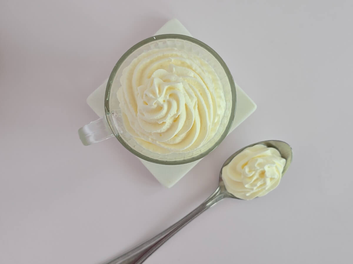 Vue de dessus d'une tasse transparente contenant une rosace de crème chantilly blanche aérienne, mettant en avant la précision du pochage à la douille.