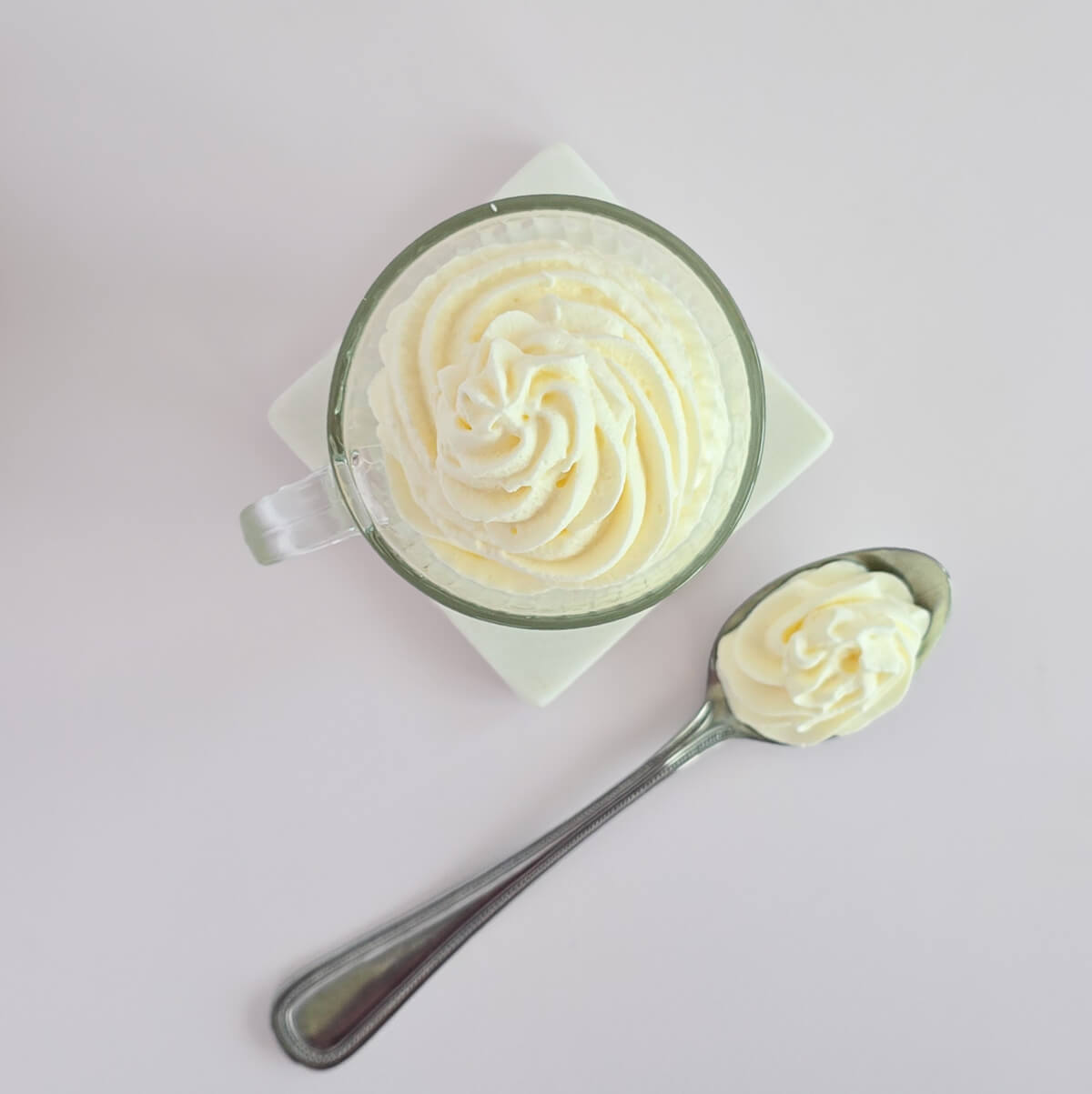 Vue de dessus d'une tasse transparente contenant une rosace de crème chantilly blanche aérienne, mettant en avant la précision du pochage à la douille.