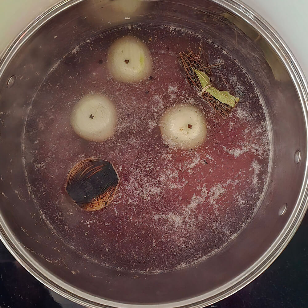 Vue de dessus d'une marmite où mijotent des oignons brûlés, du thym et des herbes dans un bouillon de bœuf ambré.