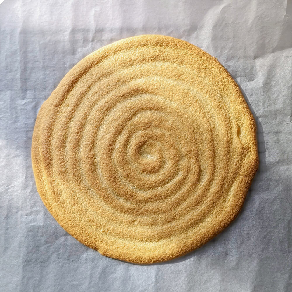 Utilisation d'une poche à douille pour pocher le biscuit cuillère en spirale, en partant du centre vers l'extérieur.