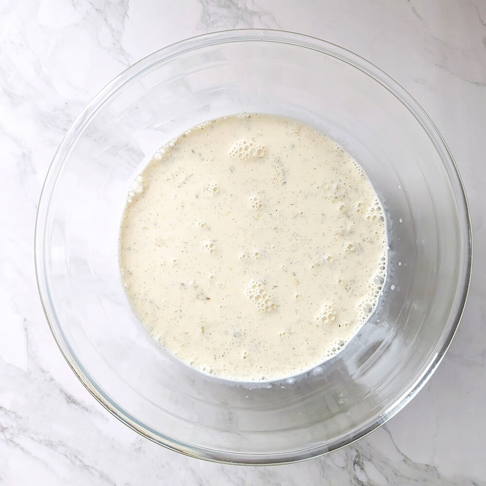 Préparation d'une ganache montée : versement de la crème liquide chaude infusée à la vanille sur le chocolat blanc pour créer l'émulsion.