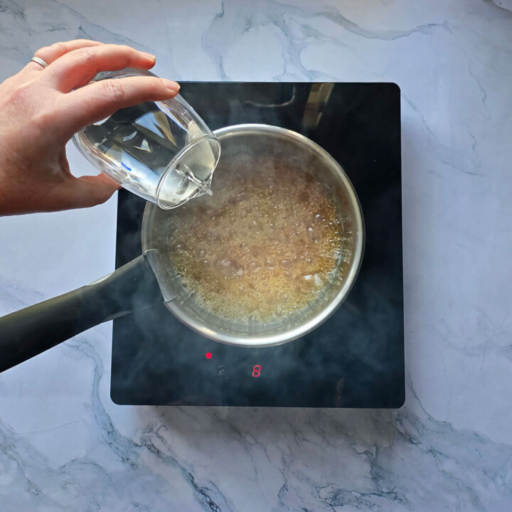 Une main versant de l'eau dans la préparation d'un caramel liquide maison.