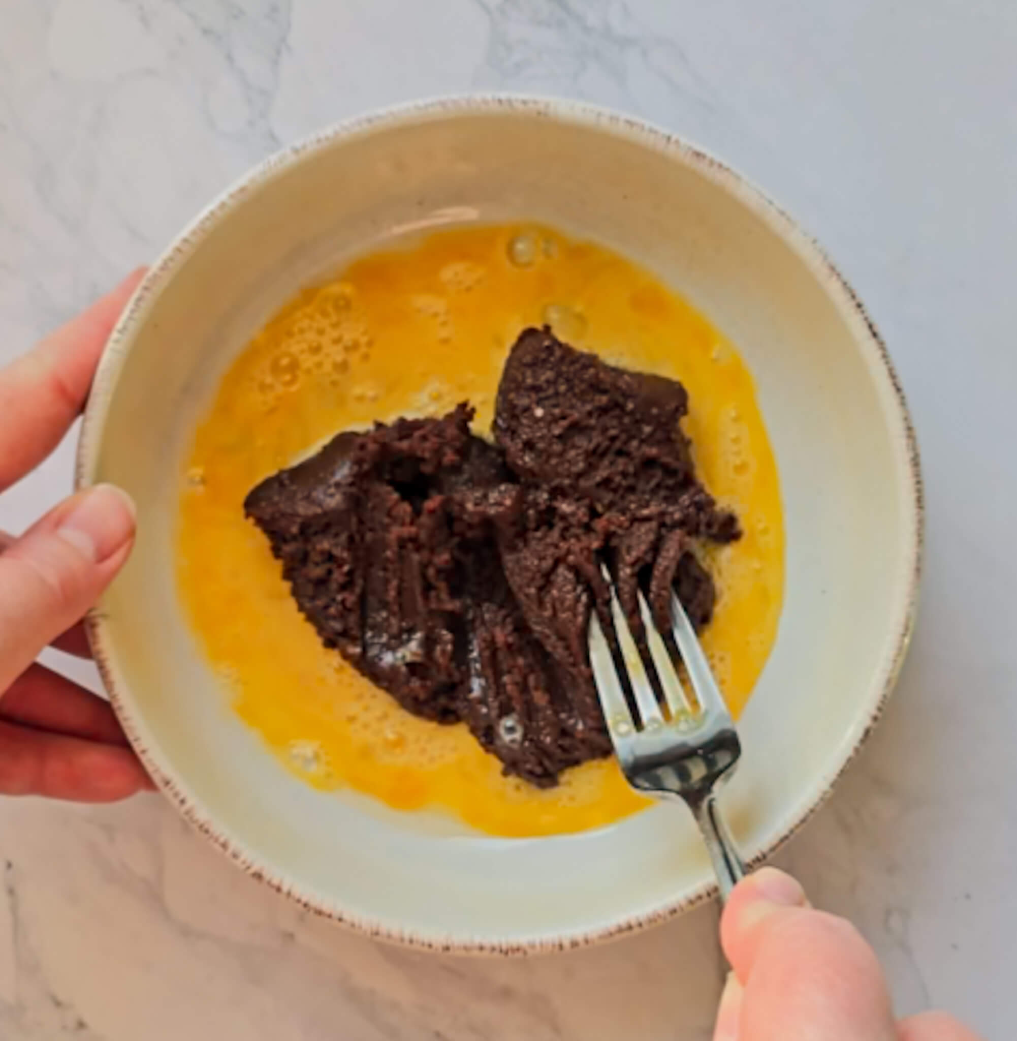 Une main fouettant un œuf et de la pâte à tartiner dans un bol pour réaliser un bowlcake chocolat noisette.