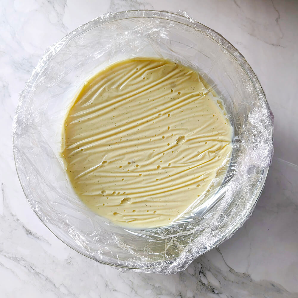 Ganache à la vanille filmée au contact avec du film étirable dans un bol en verre, prête pour un repos de 6 heures au frais avant d'être montée.