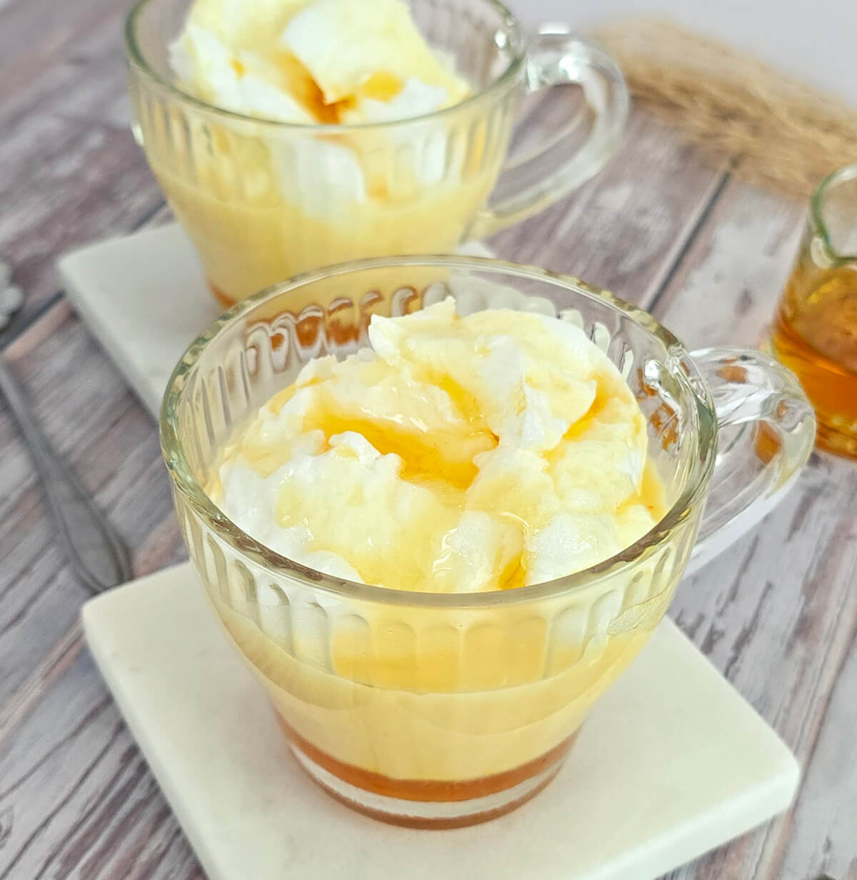 Deux îles flottantes servies dans des tasses en verre sur des sous-verres en marbre blanc, montrant les blancs en neige sur une crème anglaise onctueuse.