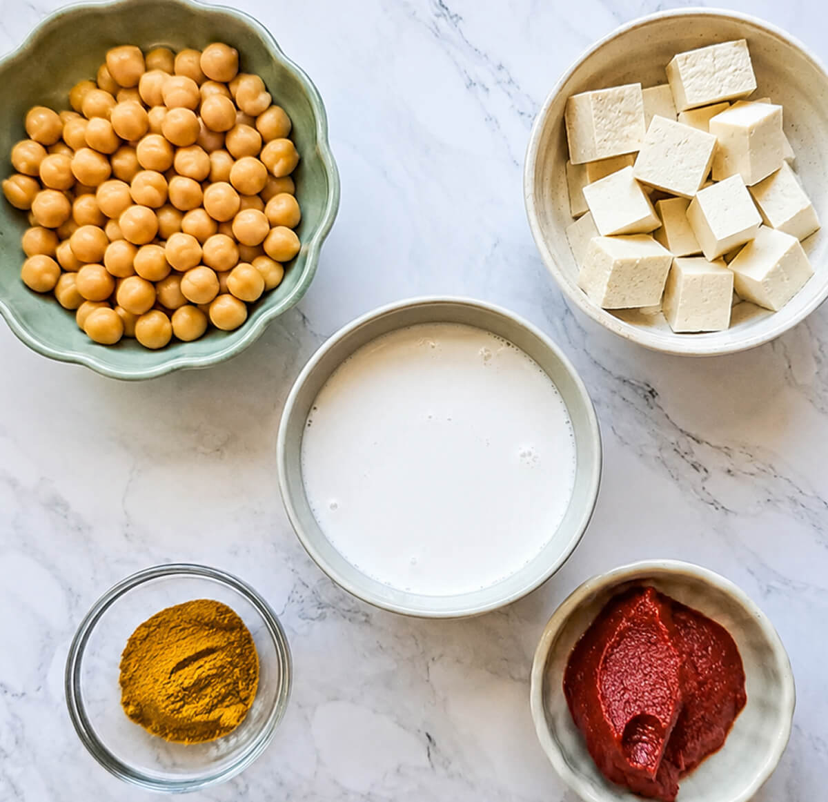 Des ingrédients pour réaliser un curry de pois chiches lait de coco, sur un fond blanc marbré.