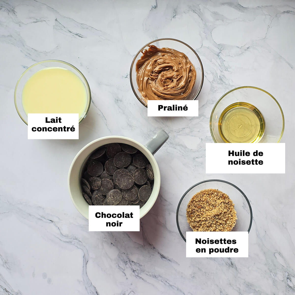 Des ingrédients pour faire une pâté à tartiner chocolat noir maison, sur un fond blanc marbré.