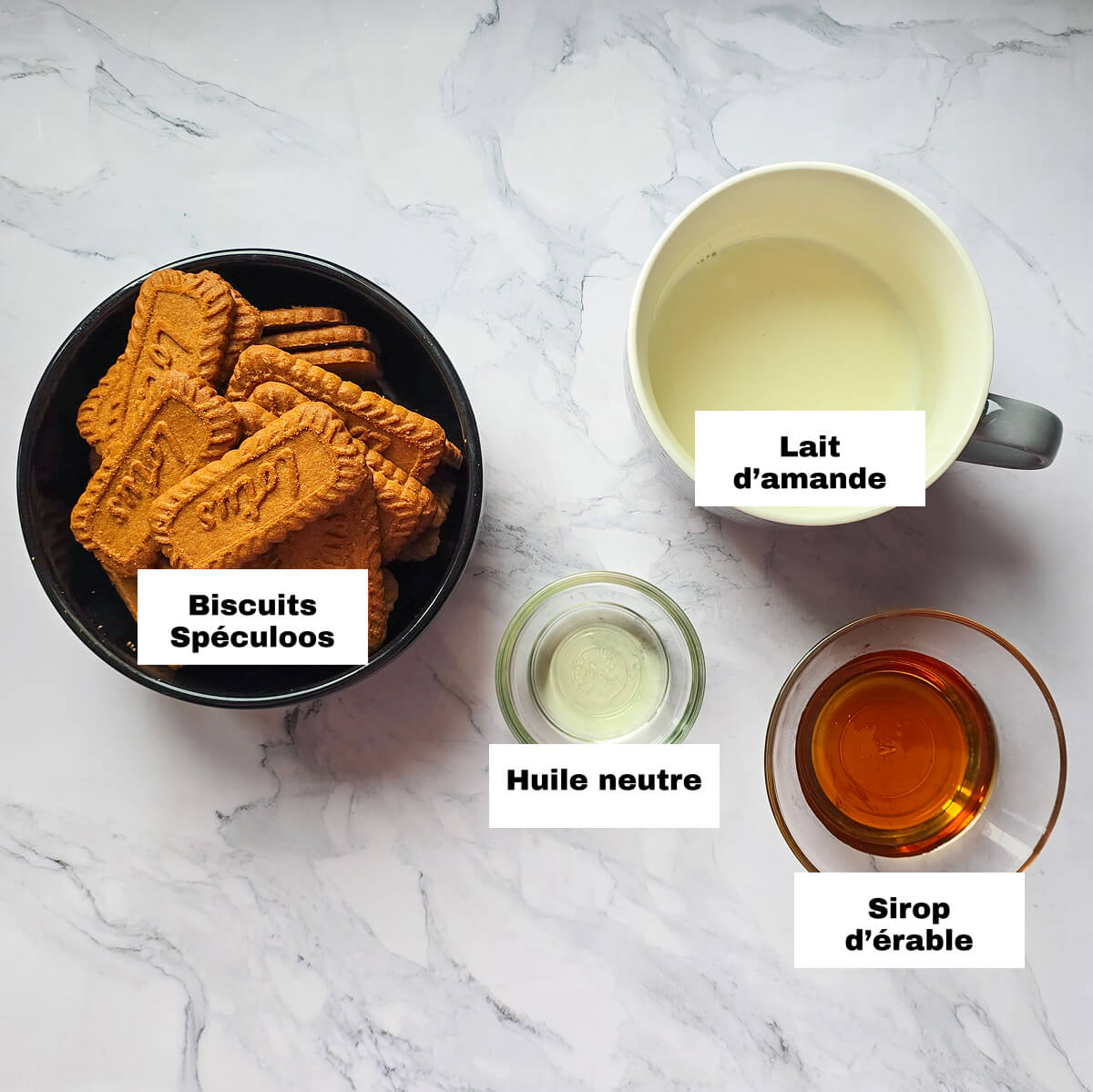 Des ingrédients pour faire une pâte à tartiner Spéculoos vegan, sur un fond blanc marbré.