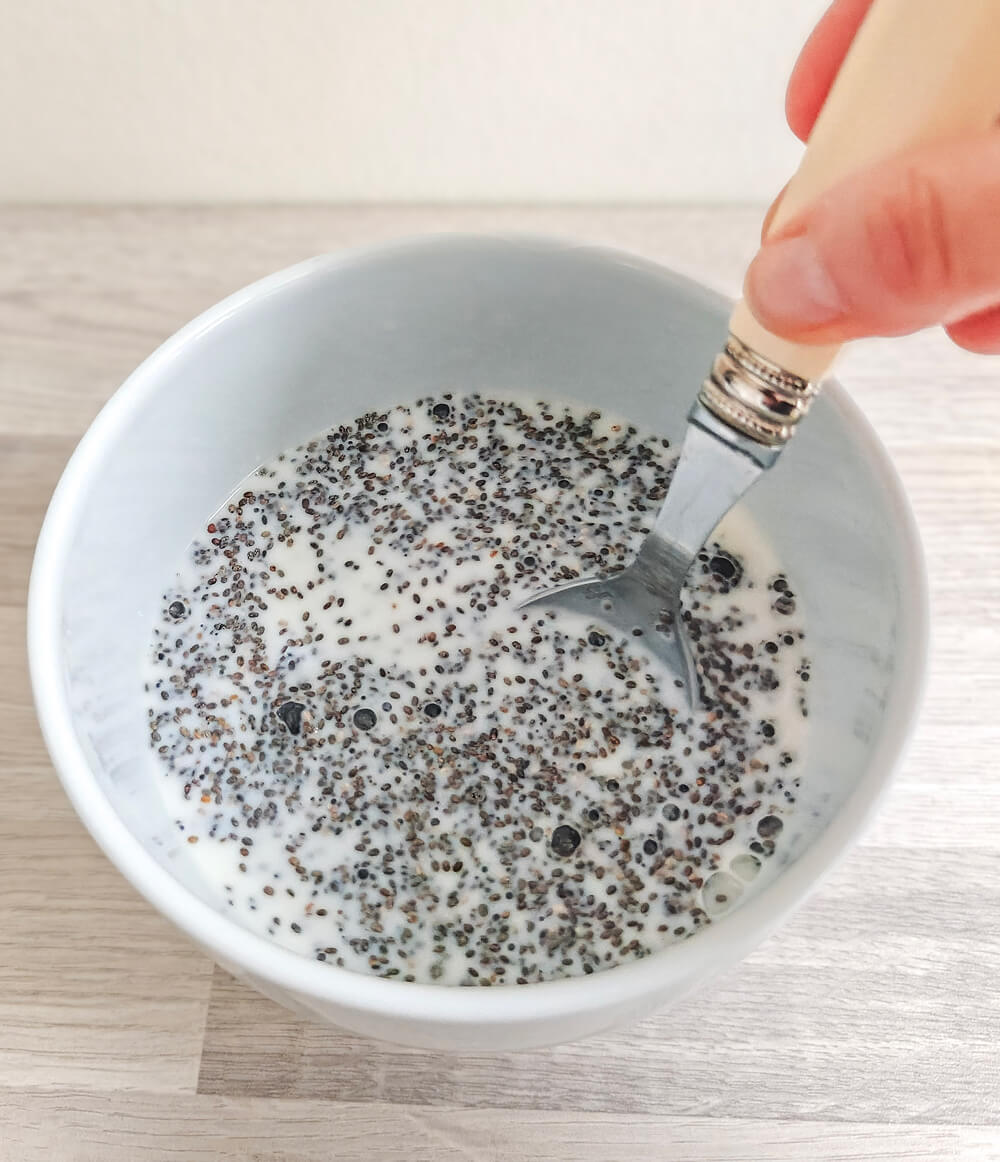 Mélange à la cuillère de graines de chia et de lait végétal dans un bol blanc pour obtenir une texture de pudding homogène.