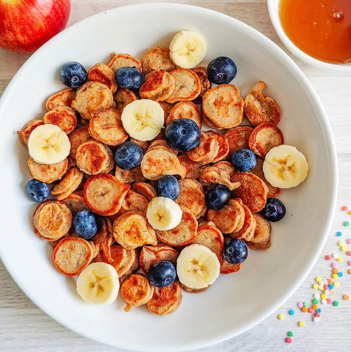 Des mini pancakes banane moelleux, dans une assiette avec des fruits.